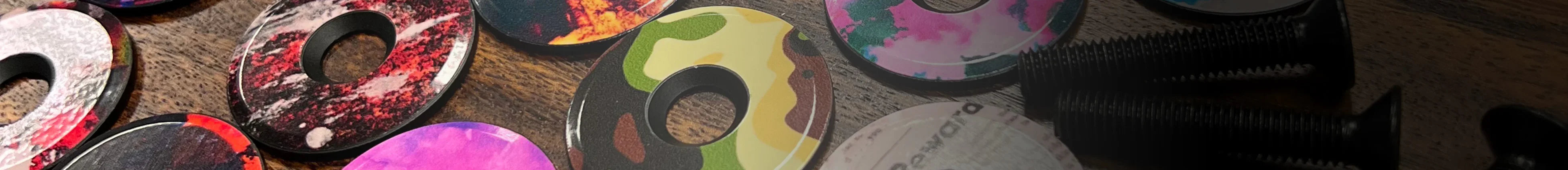 Colorful, patterned bicycle top caps and black bolts on a wooden surface.