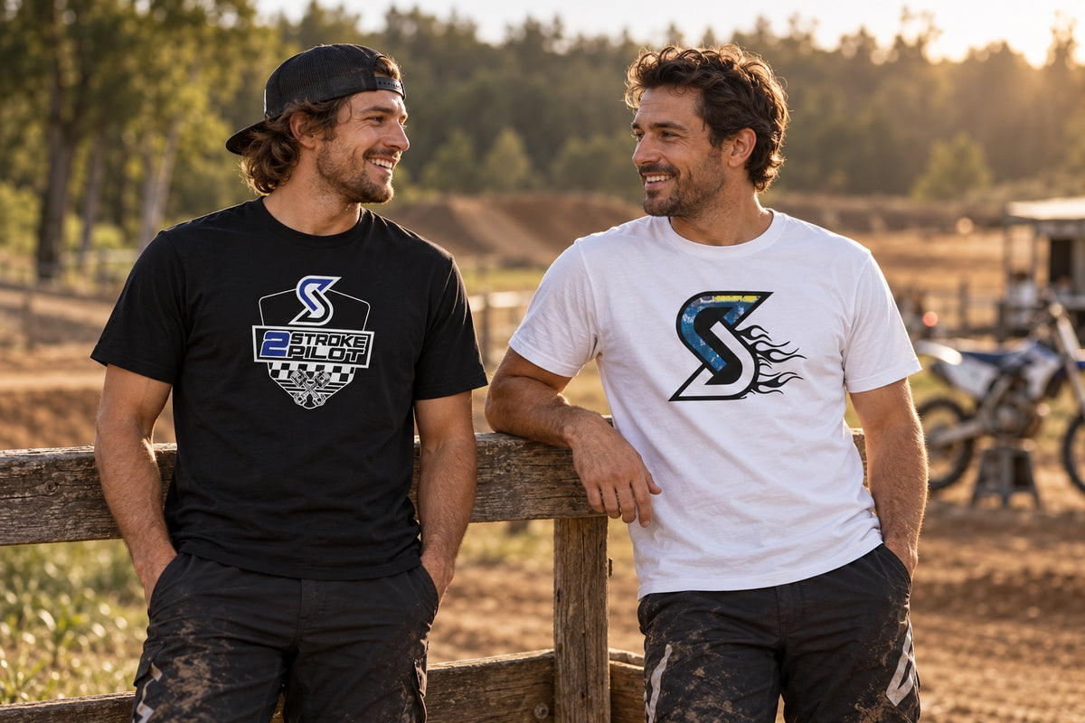 Twee mannen dragen zwarte en witte Sickstyle T-shirts met 2 Stroke Pilot- en Blue Flame-prints naast een motorcrossbaan.