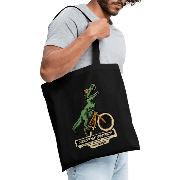 Schwarzer Baumwoll-Stoffbeutel mit T-Rex auf gelbem Fahrrad und “Sickstyle Graphics” Logo.